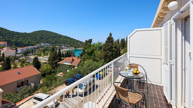 A balcony with a table and chairs, overlooking a coastal town with buildings and a clear blue sky. - A3 KABLAR'S SUNNY SUITES 1BR APT with balcony and sea view - Duplicate (Dubrovnik)