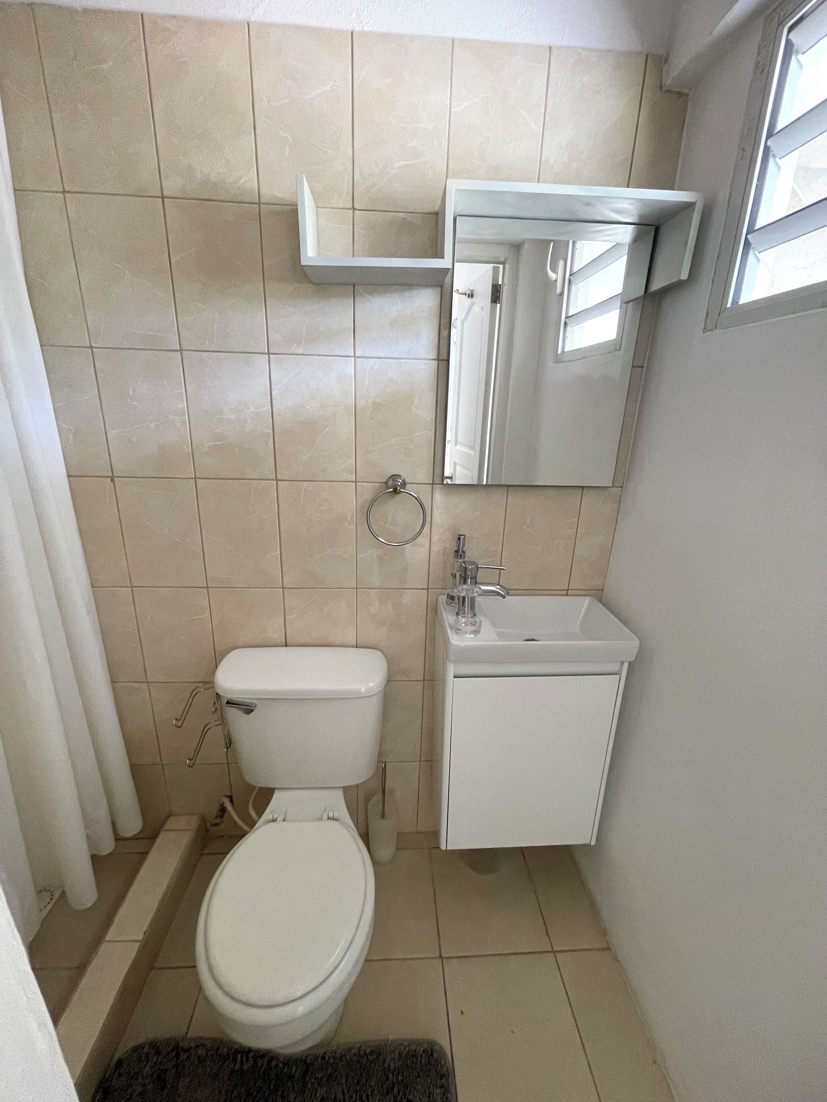 A small, clean bathroom with a toilet, sink, and mirror.