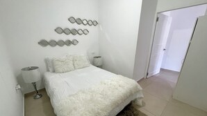 A bedroom with a bed, two bedside lamps, a fluffy rug, and a wall-mounted decorative piece. - Rommar Cozy Suite (CAY HILL ,LITTLE BAY)