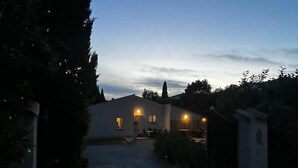 A driveway leading to a house with a gated entrance, surrounded by trees and a clear sky.