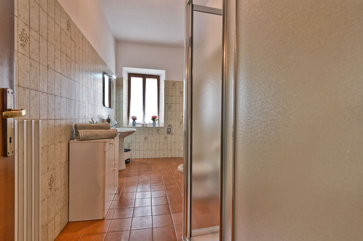 A narrow hallway with a bathroom on the left, featuring a toilet, sink, and towel rack.