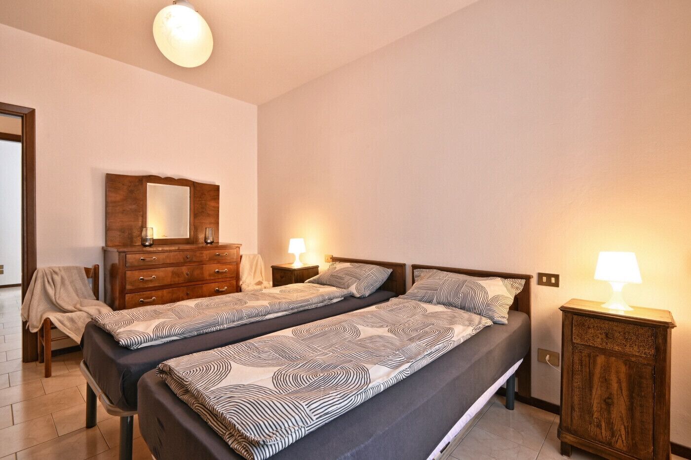 Una camera da letto con due letti, una cassettiera, uno specchio e due lampade da comodino.