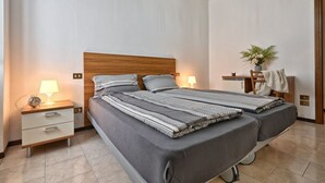 Ein Doppelbett mit Holz Kopfteil, zwei Nachttische mit Lampen, eine kleine Pflanze und ein Stuhl mit Handtuch.