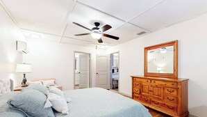 Un dormitorio con cama, cómoda de madera, ventilador de techo y espejo.