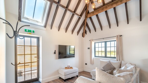 A room with a wooden ceiling, a TV mounted on the wall, a sofa with cushions, and a window with curtains. - Corley Rocks Barn - UK45939 (Corley)