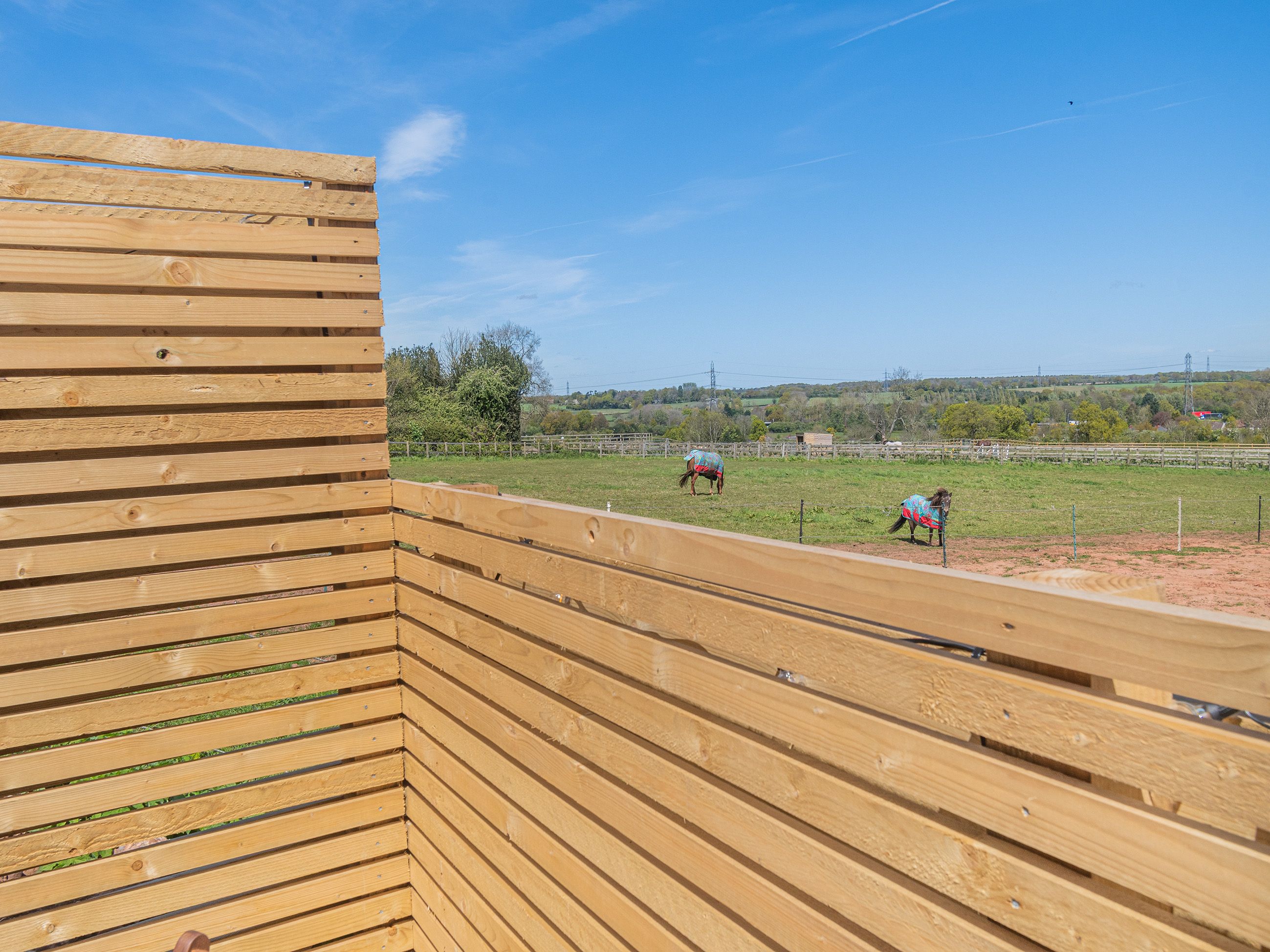 A wooden fence with a clear view of a fenced pasture with horses.