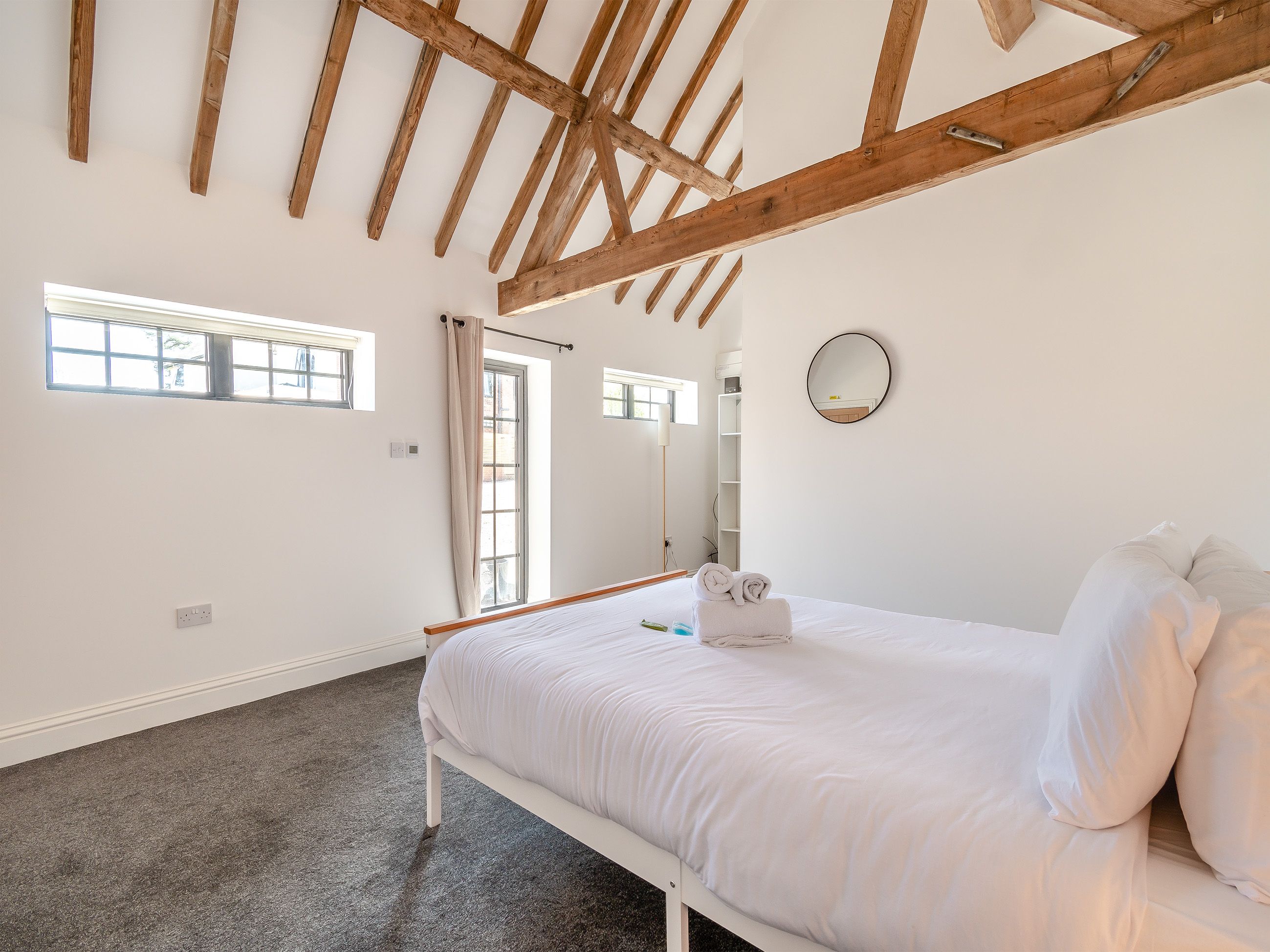 Un dormitorio con cama, ventana, espejo y techo con vigas de madera.