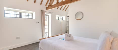 A bedroom with a bed, a window, a mirror, and a ceiling with wooden beams.