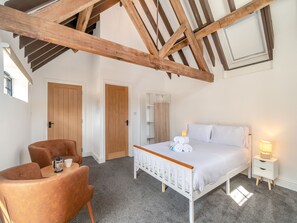 Un dormitorio con techo de madera, una cama con ropa de cama blanca, una mesita de noche con una lámpara y una silla con cafetera.