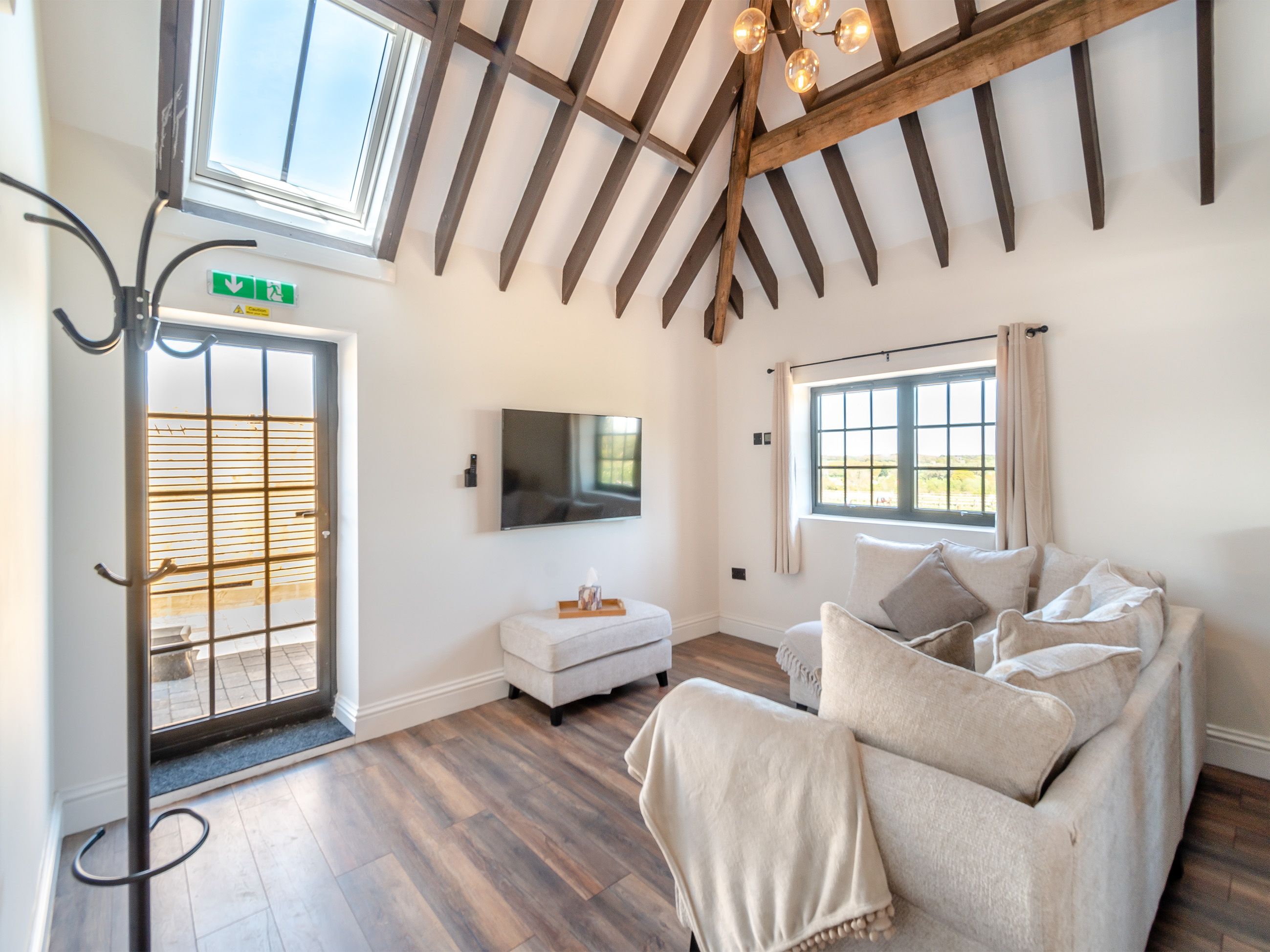 Une pièce avec un plafond en bois, un téléviseur fixé au mur, un canapé avec des coussins et une fenêtre avec des rideaux.