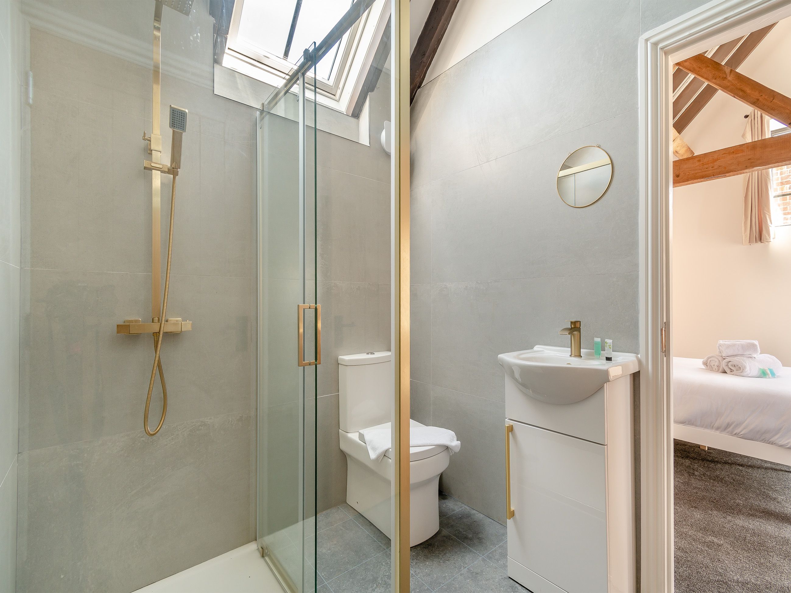 Un baño moderno con cabina de ducha de vidrio, inodoro blanco y lavamanos con espejo.