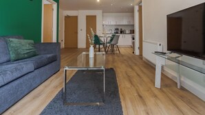 Een moderne woonkamer met een grijze bank, een glazen salontafel en een tv op een glazen voetstuk.