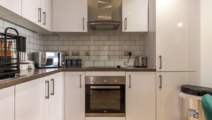 Een moderne keuken met witte kastjes, een roestvrijstalen oven, een koffieapparaat en een prullenbak.