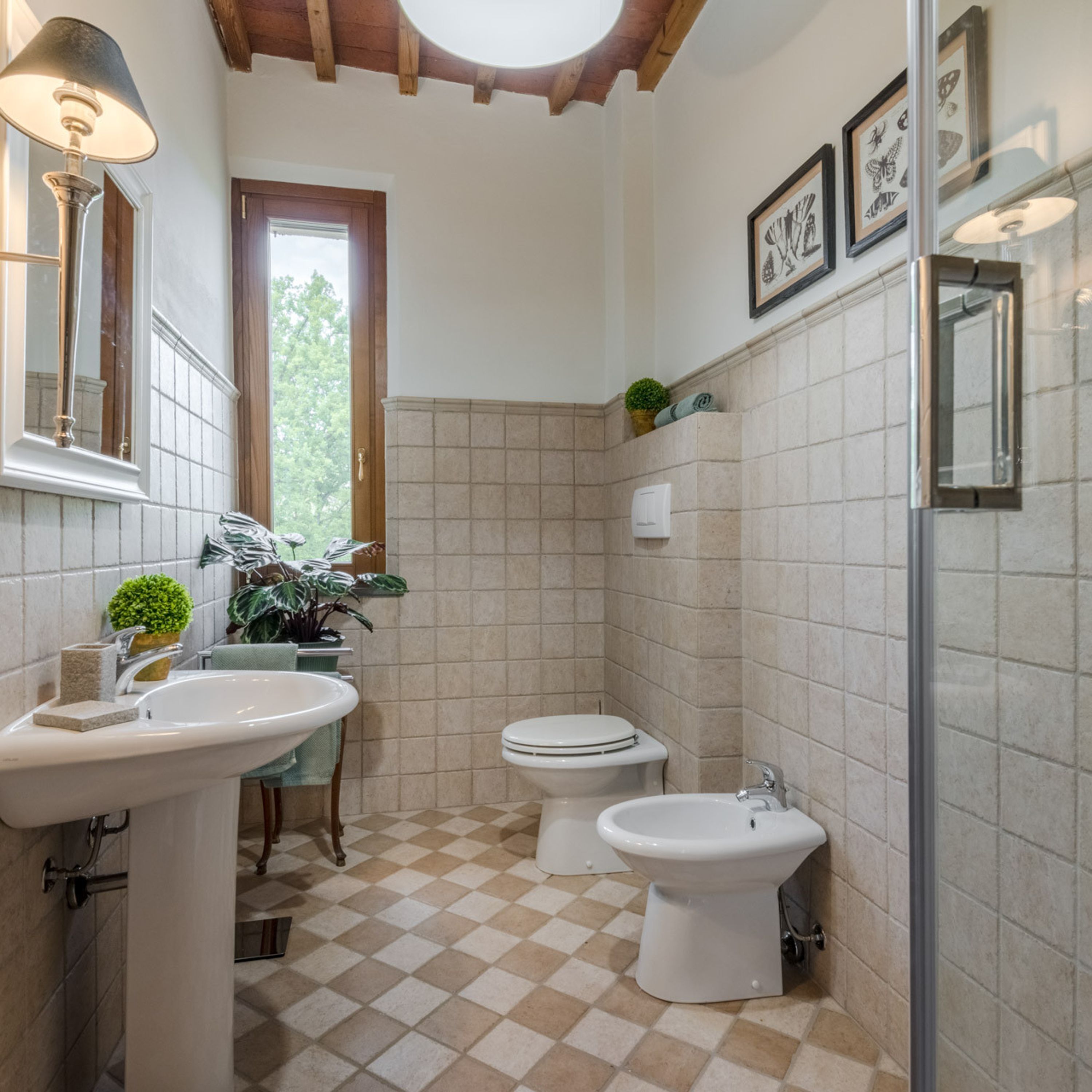 A bathroom with a checkered floor, a sink, a toilet, a bidet, and framed artwork on the wall.