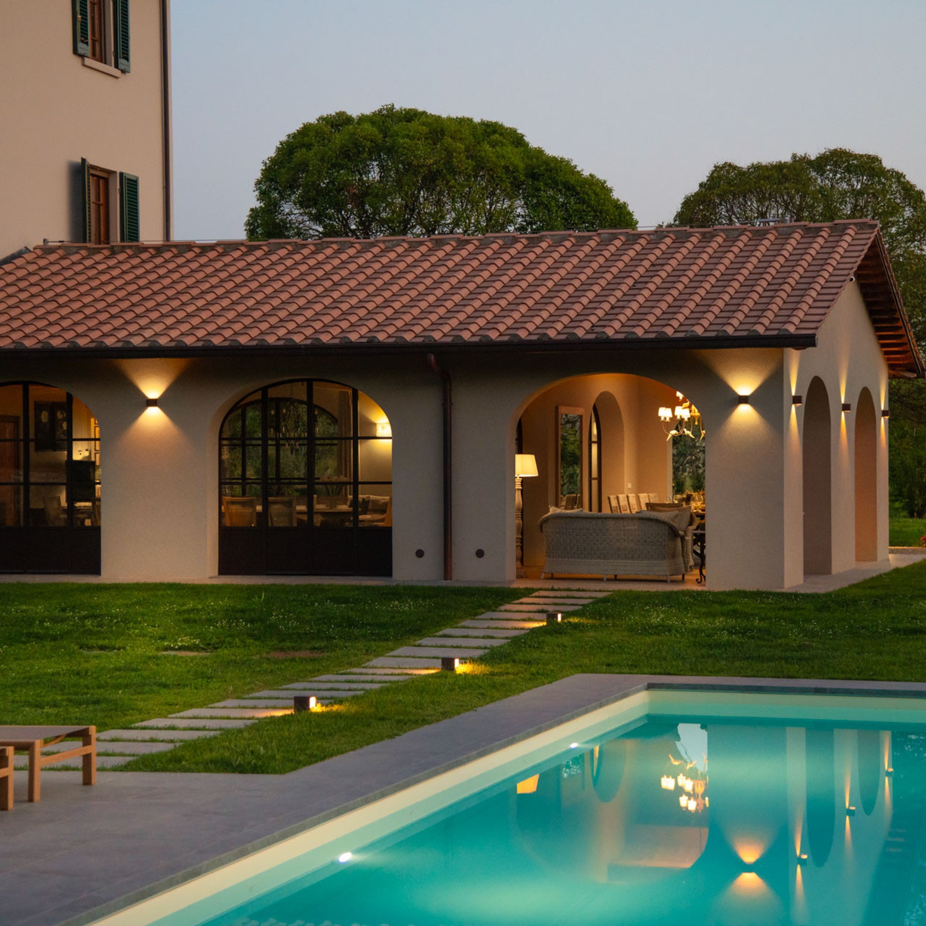 Une maison moderne dotée d’une piscine, avec un patio aménagé avec du mobilier d’extérieur et une entrée bien éclairée.
