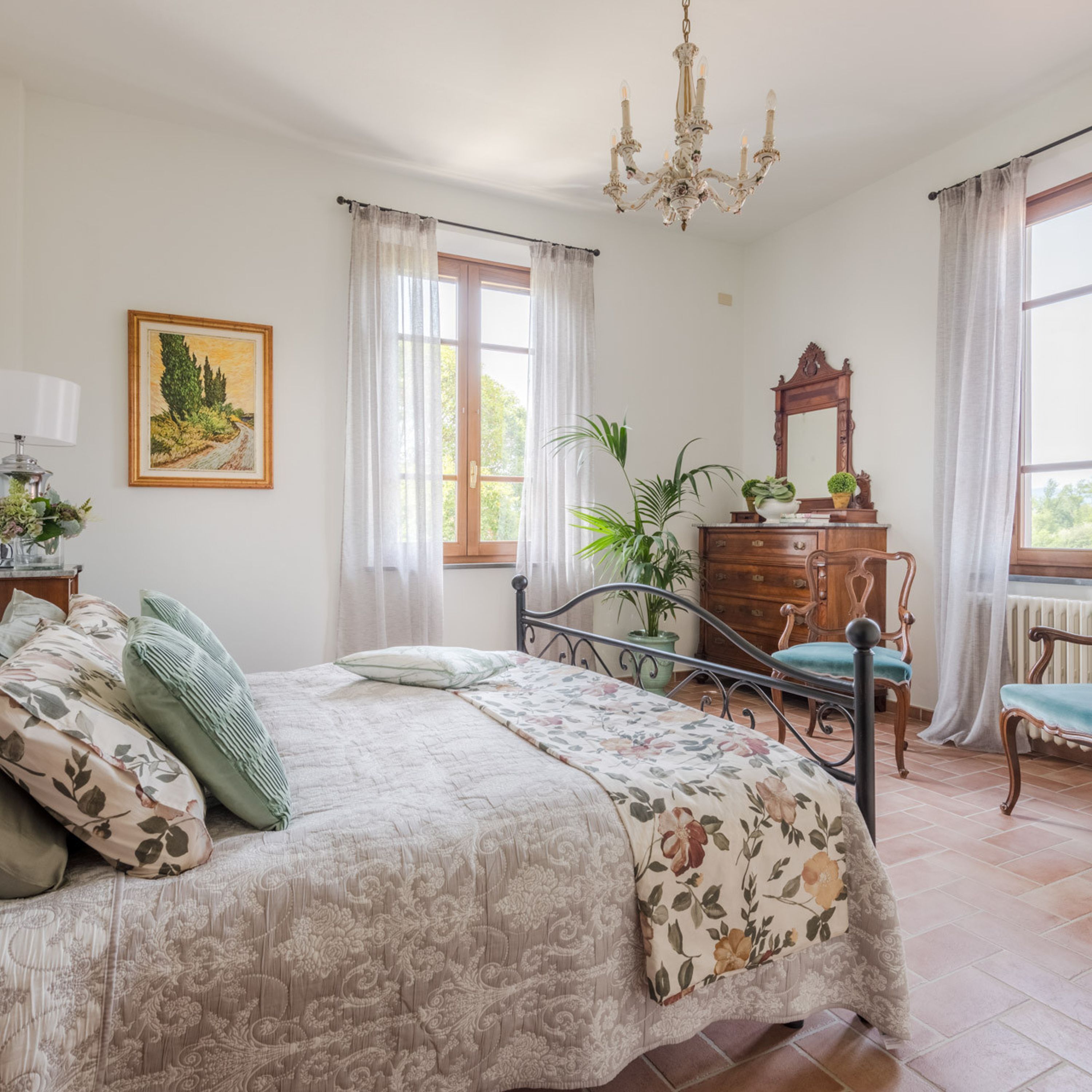 Ein Schlafzimmer mit einem Bett, einem Schminktisch, einem Sessel, einem Spiegel, einer Chandelier und einem Fenster mit Vorhängen.
