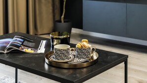 A modern living room with a black coffee table, a magazine, a tray with a cup and macarons, a potted plant, and a TV on the wall. - Luca (Bucharest)
