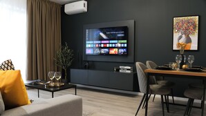 A modern living room with a flat-screen TV mounted on the wall, a dining area with a table and chairs, and a sofa with a yellow pillow. - Luca (Bucharest)
