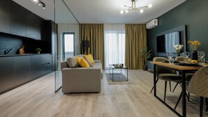 A modern living room with a sofa, dining table, and a TV. There is a kitchen area with cabinets and a window with curtains. - Luca (Bucharest)