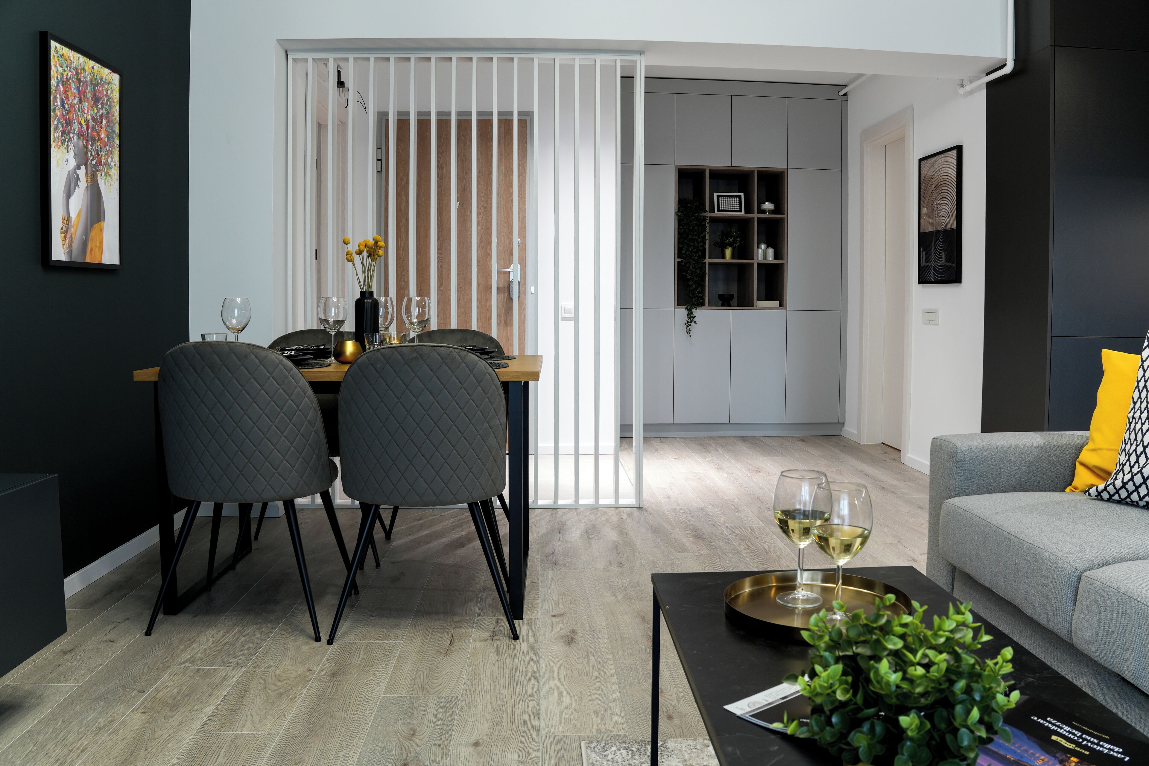 Un salon moderne avec un canapé gris, une table basse agrémentée d’une plante, et un coin repas comprenant une table et des chaises.