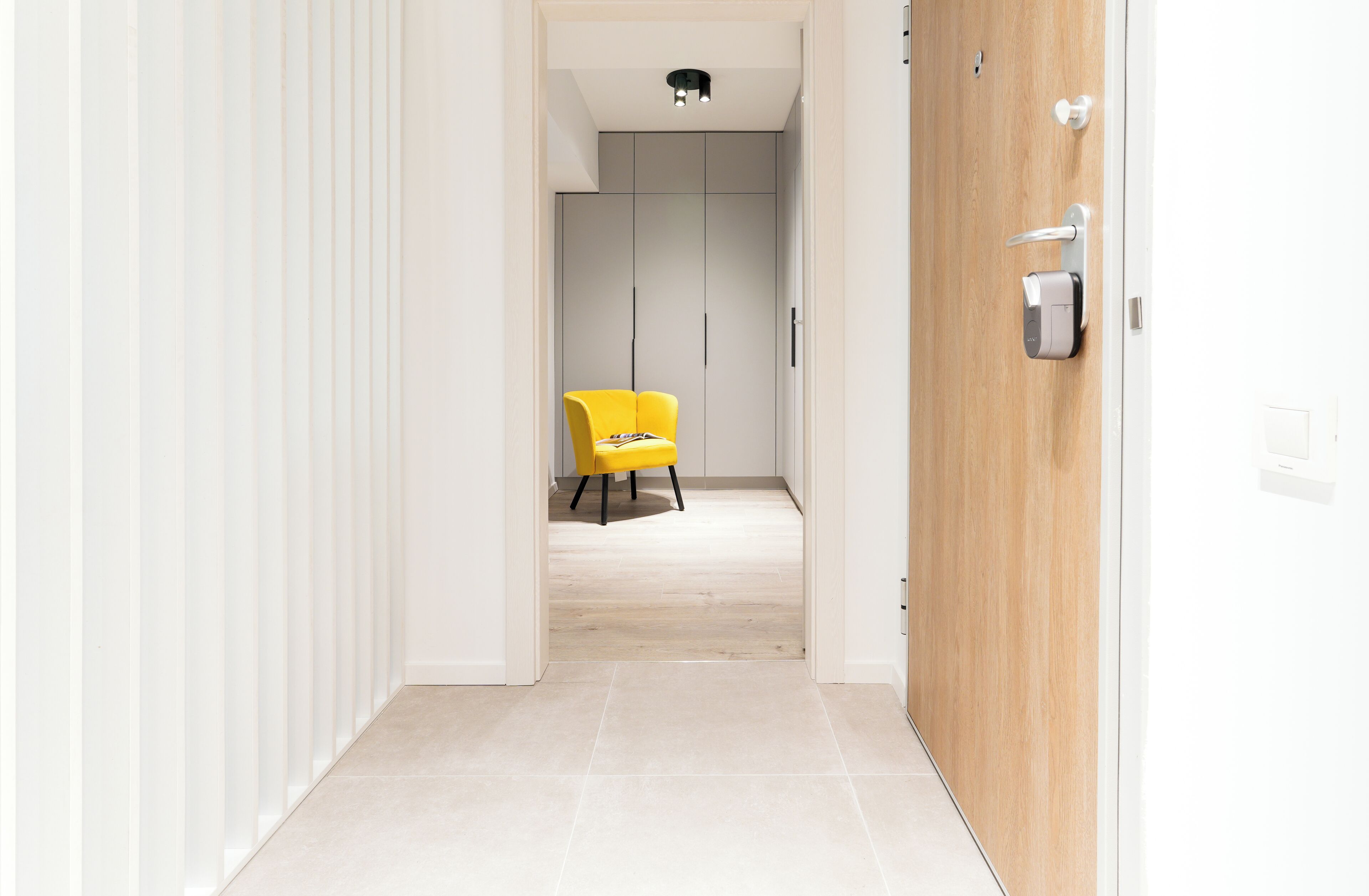 A hallway with a yellow chair, a wooden door, and a white wardrobe.