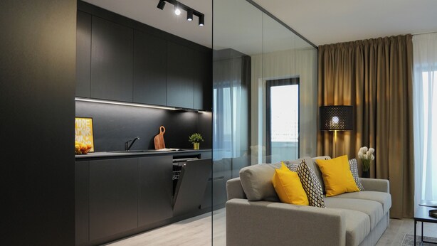 A modern living room with a sofa and a glass partition separating it from a kitchen area. - Luca (Bucharest)