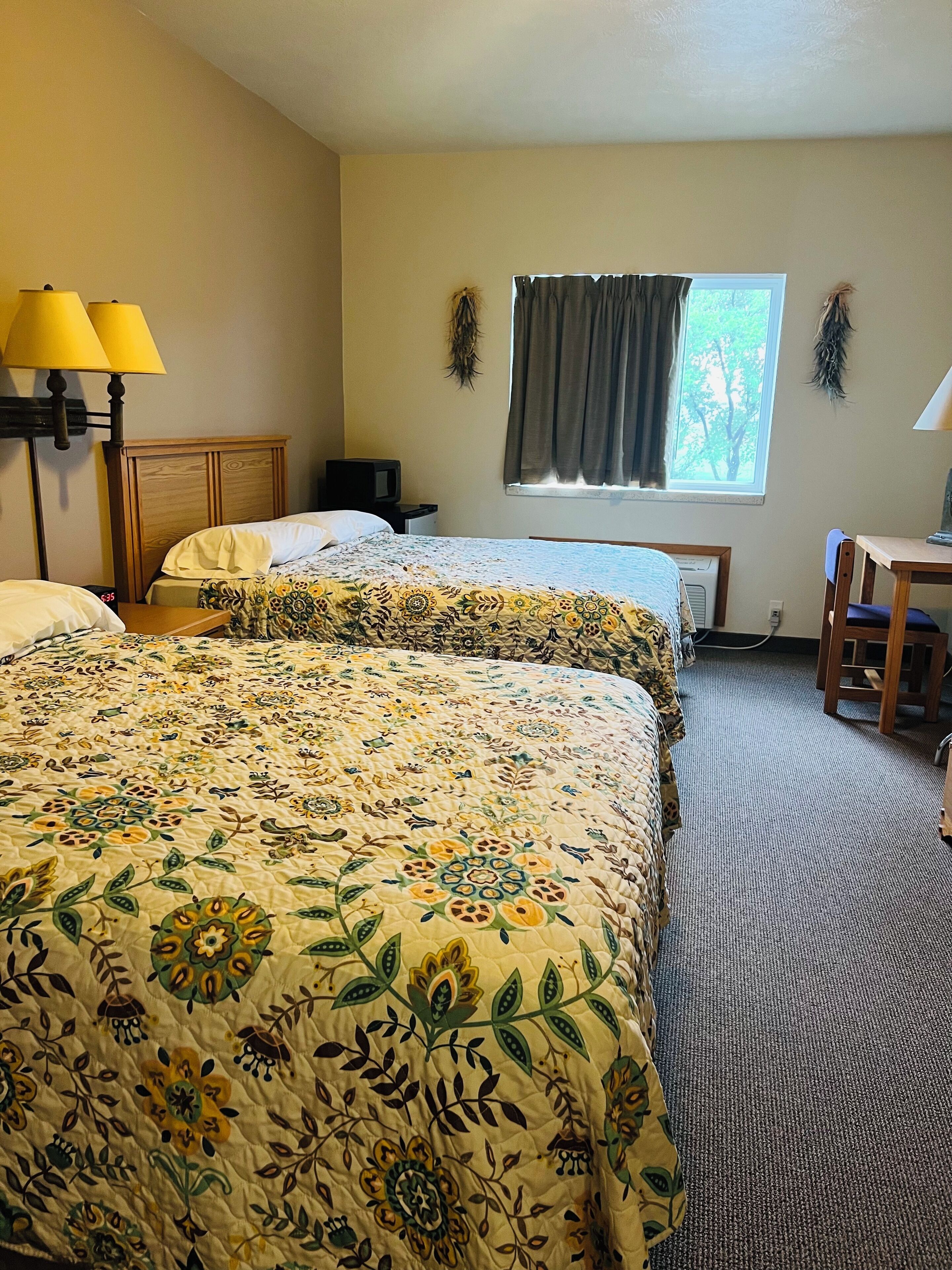 A hotel room with two beds, a desk, a chair, a TV, and a window with curtains.