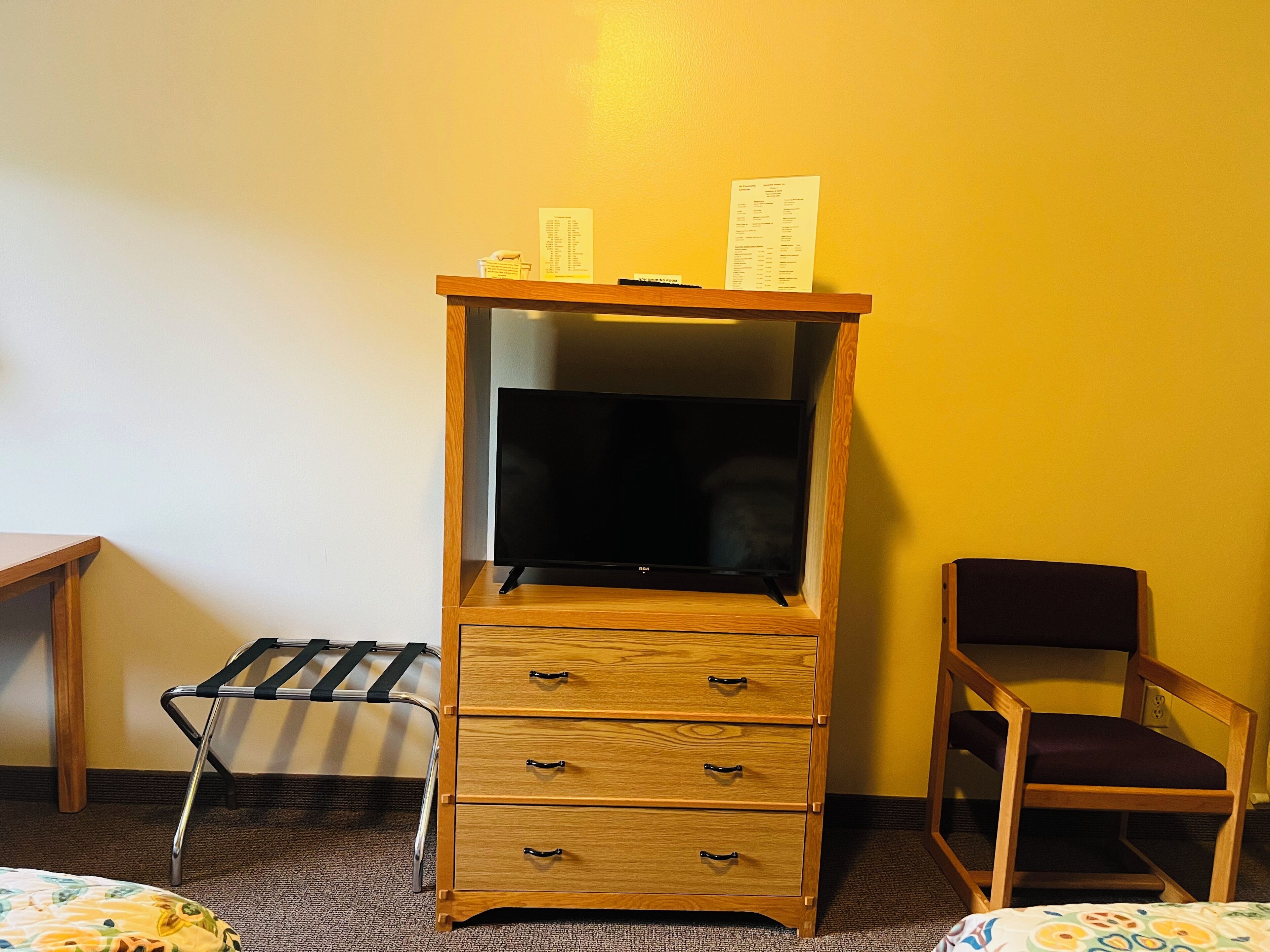 Un meuble en bois avec des tiroirs, un téléviseur, une chaise et une petite table avec un plateau.