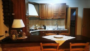 A kitchen with wooden cabinets, a tiled backsplash, a dining table with chairs, and a lamp. - 1 Bedroom Apartment in Procida (Procida)