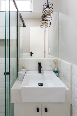 Un baño con lavamanos blanco, cabina de ducha con mampara de vidrio y espejo con luz.