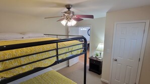 Une chambre avec un lit superposé, un ventilateur de plafond, une porte et une table de chevet avec une lampe.
