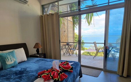 A bedroom with a bed, a nightstand, a lamp, and a view of an outdoor patio with a table and chairs.