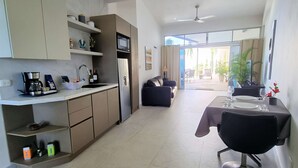 A modern kitchen with a built-in oven, a coffee maker, and a refrigerator. There is a dining area with a table and chairs, and a sofa. - S9 - Vista Ocean Suites (Quepos)