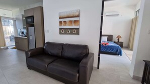 A modern living room with a leather sofa, a kitchen area with a refrigerator, and a bedroom with a bed and curtains. - S9 - Vista Ocean Suites (Quepos)