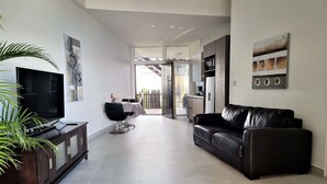 A modern living room with a flat-screen TV, a leather sofa, and a dining area with a table and chairs. - S9 - Vista Ocean Suites (Quepos)