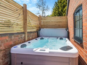 A hot tub in a backyard with a wooden fence, brick wall, and a window. - Fountain Front Barn - UK45937 (Corley)