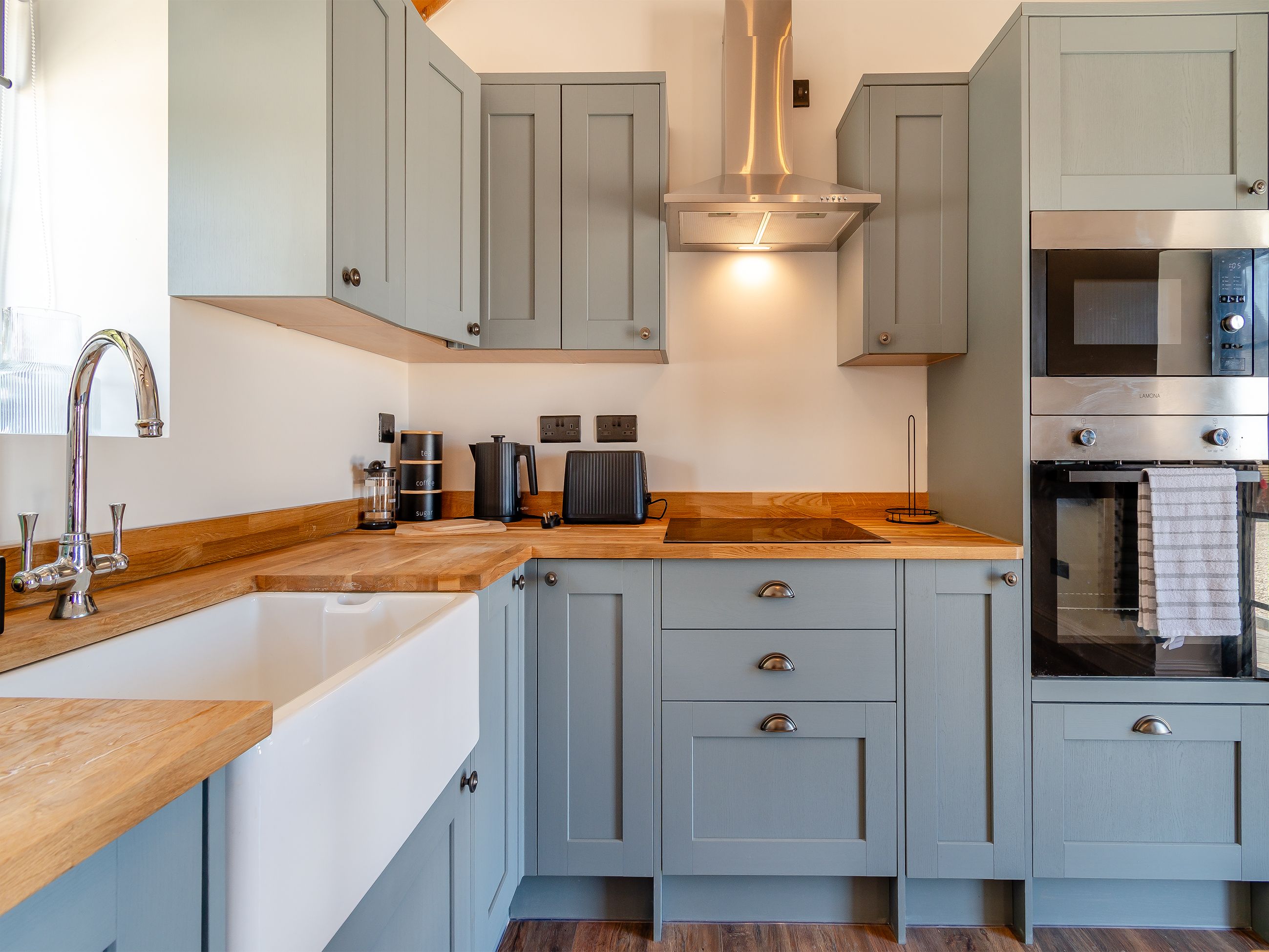 A modern kitchen with grey cabinets, a wooden countertop, a stainless steel range hood, and a built-in oven.