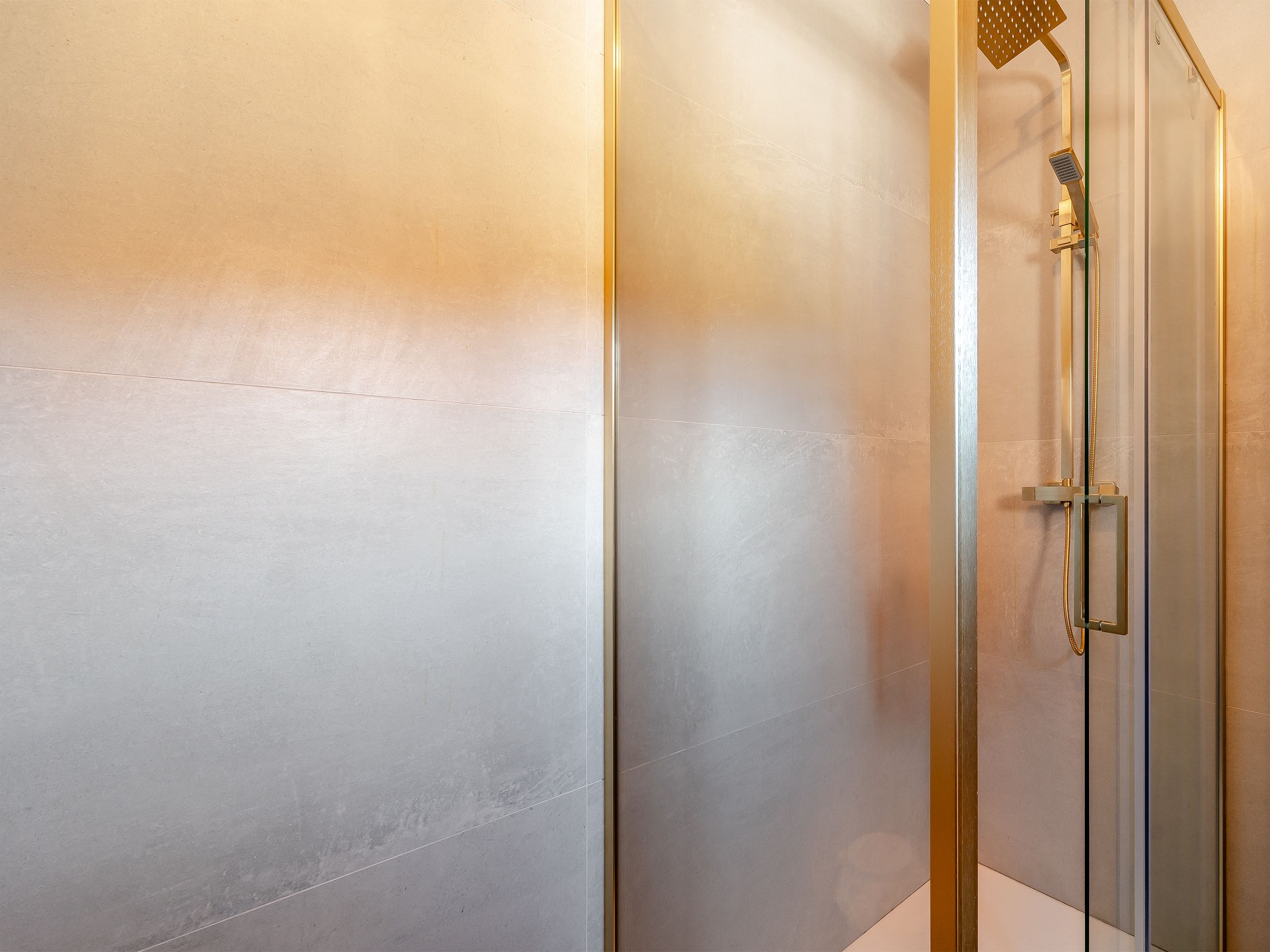 Un área de ducha moderna con puerta de cristal y ducha con cabezal dorado.