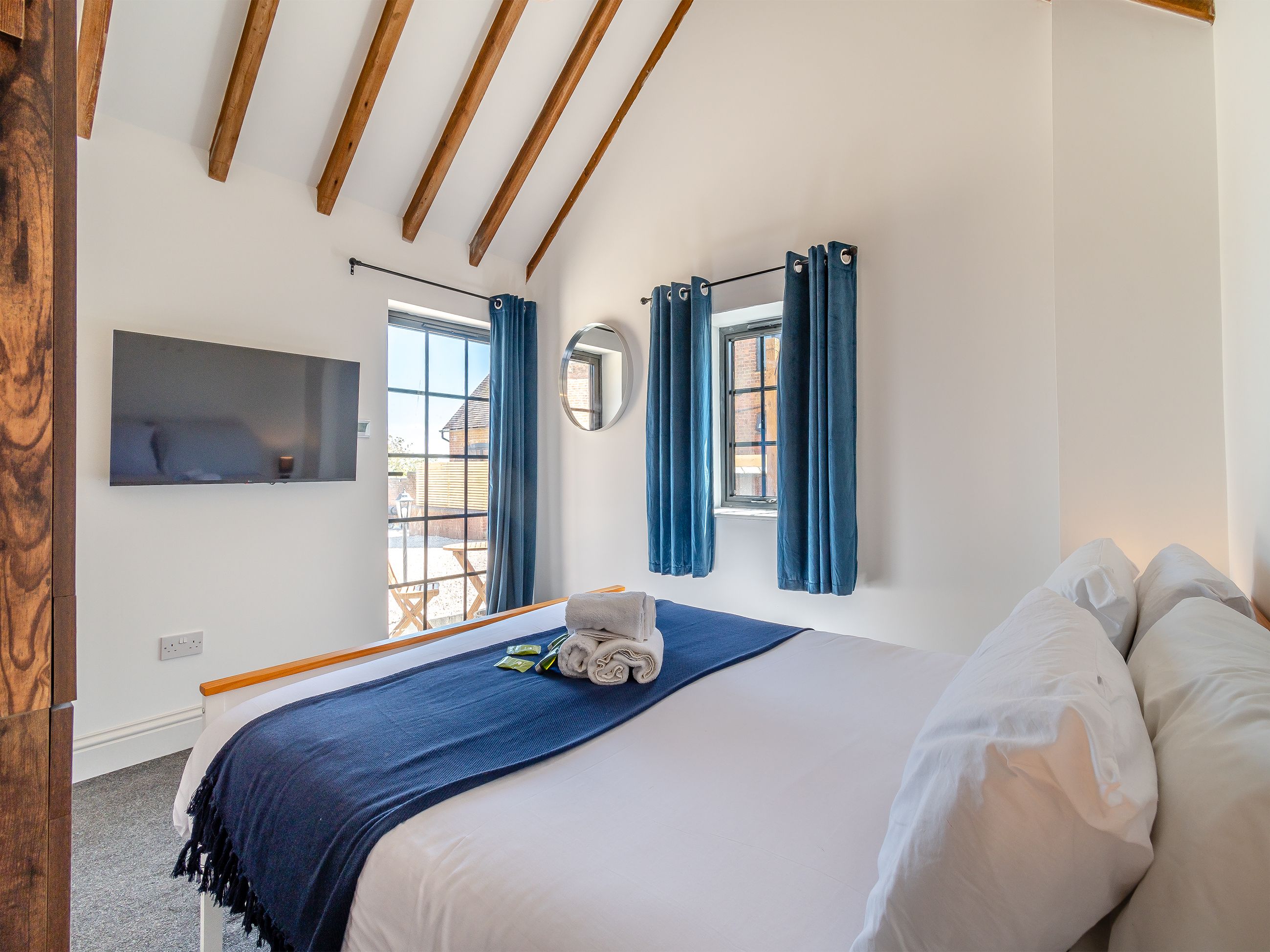 A bedroom with a large bed, a TV mounted on the wall, and a window with curtains.