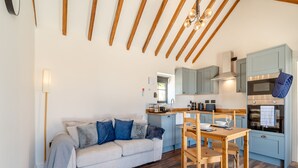 Una cocina moderna con vigas de madera, un comedor con mesa y sillas, y una sala de estar con sofá.