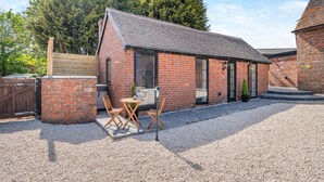 A brick building with a sloped roof, a gravel courtyard, and a wooden table with chairs. - Fountain Front Barn - UK45937 (Corley)