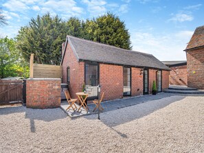 A brick building with a sloped roof, a gravel courtyard, and a wooden table with chairs. - Fountain Front Barn - UK45937 (Corley)
