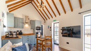 A modern kitchen with wooden beams, a dining area with a table and chairs, and a TV mounted on the wall. - Fountain Front Barn - UK45937 (Corley)