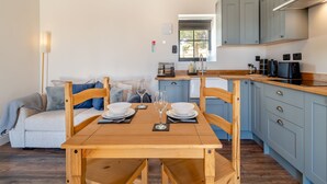 A modern kitchen with wooden beams, a dining table set for two, and a cozy seating area with a sofa and cushions. - Fountain Front Barn - UK45937 (Corley)