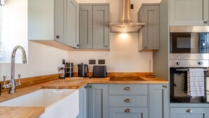 Una cocina moderna con armarios grises, encimera de madera, campana extractora de acero inoxidable y horno empotrado.