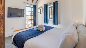 Un dormitorio con una cama grande, un televisor montado en la pared y una ventana con cortinas.