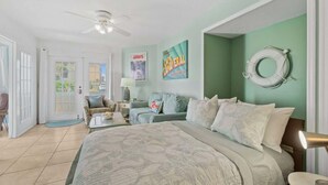 A bedroom with a bed, a ceiling fan, a wall-mounted life preserver, and a door leading to a balcony. - Ground Floor | Oceanfront Patio | Resort Style | P (Cape Canaveral)