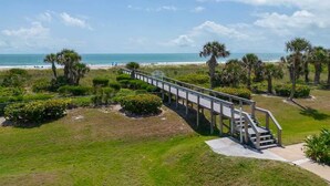 A pathway leading to a beach with palm trees and a clear sky. - Ground Floor | Oceanfront Patio | Resort Style | P (Cape Canaveral)