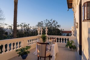 Un balcon avec une table dressée pour le dîner, des plantes en pot et une vue sur les arbres et les montagnes.