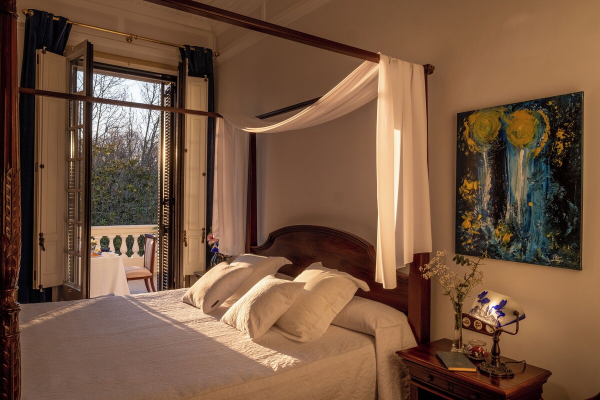 Un lit à baldaquin avec du linge de lit blanc, une table de chevet en bois avec une lampe et un tableau accroché au mur.